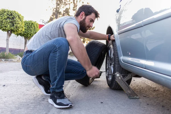 handsome guy using a car jack to lift a car and change a flat tire and put spare tire