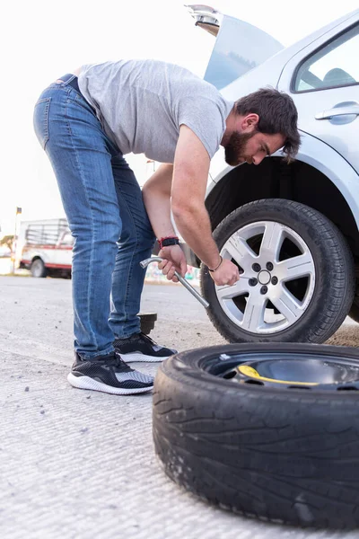 young man loosening a nut of his car tire, changing a flat tire on the road