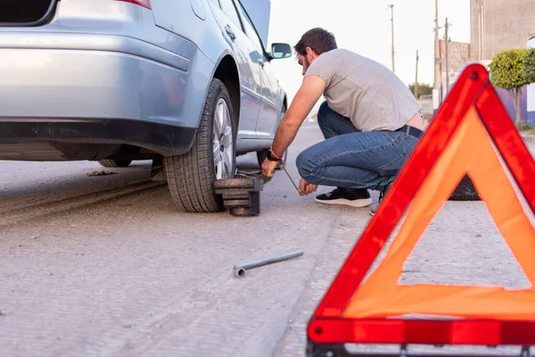 worried man changing a flat tire, car with opened trunk taking spare tire