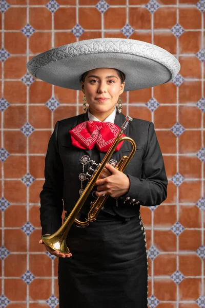 female mexican mariachi trumpetist woman smiling using a traditional mariachi girl suit on a talavera background. good looking latin hispanic trumpet player musician feminine using a hat