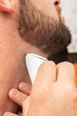 Tıraş olurken ve sakalını elektrikli tıraş bıçağıyla keserken aynada bıyık keserken.