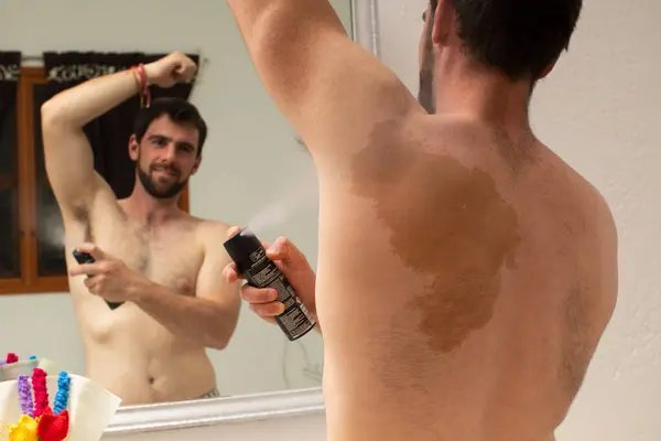 Çekici bir genç adam vücuduna parlak bir deodorant sürüyor, çeşitli deri lekeleri ve benleri olan genç bir adam, tenimde çok mutlu hissediyorum.
