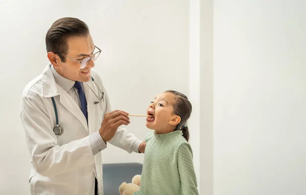 latin doctor checking girl throat using a tongue depressor. Hispanic smiling pediatrician examining kid sore throat, child at doctor\'s office