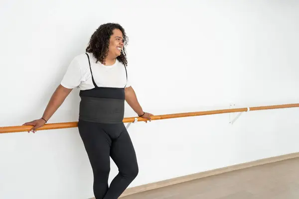 Kendine güvenen genç erkek dansçı dinlenirken gülümsüyor ve bale barına yaslanıyor. Çekici, iri yarı, Afro-Amerikan bir adam gülüyor.