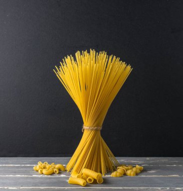 Bir demet spagetti ve ahşap bir masada değişik türde makarna..