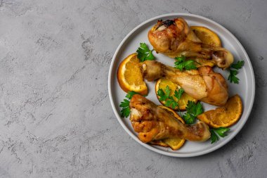 Bal soslu tavuk bacağı, gri tabakta portakallar ve gri arka planda. Metin için yeri var. Yukarıdan görüntüle.