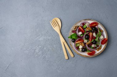 Kiraz domatesli salata, karışık salata yeşili, ceviz, kızılcık, siyah zeytin ve soya peyniri gri beton bir masada tahta kaşık ve çatalla. Sağlıklı yeme kavramı.