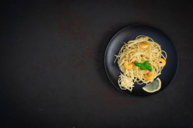 Karides ve fesleğen yapraklı spagetti ve siyah tabakta parmesan peyniri ve beton masa. Metin için boşluk olan üst görünüm.