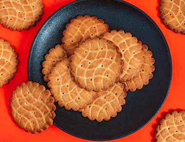 Siyah bir tabakta, parlak turuncu bir arka planda taze pişmiş kurabiyelerin yakın çekimi. Altın kurabiyeler mükemmel pişmiş, bu da onları karşı konulmaz yapıyor..