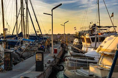 İsrail, Jaffa - 15 Aralık 2024. Jaffa 'da demir atmış yatları olan, gün batımının parlak sarı ışığında yıkanan köprü. Köprüde bir adam duruyor, parlak gökyüzüne karşı siluet.