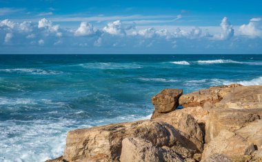 Akdeniz kayalık bir kıyı ile karşılaşıyor, gökyüzü baş döndürücü bulutlarla boyanmış, dramatik ve sakin bir manzara yaratıyor. Huzurlu sular ve bulutlarla dolu gökyüzü nefes kesici bir manzara sunuyor..