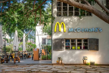 İsrail, Tel Aviv - 14 Ocak 2025 Sarona, Tel Aviv 'de McDonald' s. Gri panjurlu beyaz bir bina, ağaçların altında mobilyaları olan teras, tarihi bir alanda samimi yeşil bir ortam..
