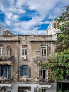 Kabuğu soyulmuş eski bir bina, açık panjurlu pencereler, çiçekli balkonlar, bulutlu parlak mavi bir gökyüzünün arka planı. Eski şehrin şehir cazibesi.