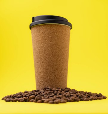 Siyah kapaklı yeniden kullanılabilir kahve fincanı ve parlak sarı arka planda dağınık kahve çekirdekleri. Sürdürülebilir içecek takımı konsepti.