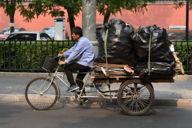 Bir adam 27 Haziran 2019 'da Pekin, Çin' de bir şehir merkezi caddesi boyunca karton ve çöp taşıyan bir triportöre biniyor..
