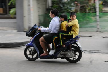 Şehirde çocuklarıyla motosiklet süren Asyalı bir kadın.