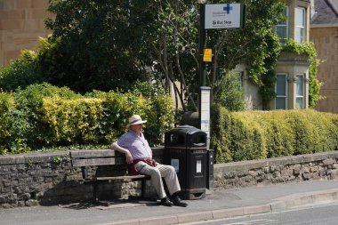 8 Haziran 2023 'te Bath, İngiltere' de otobüs beklerken bir bankta oturan yaşlı bir adam. Somerset şehrine çoğu caddede otobüs durakları bulunan geniş bir toplu taşıma ağı hizmet vermektedir..