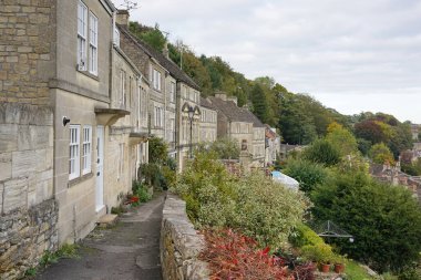 İngiltere 'nin Wiltshire şehrinde tarihi Bradford kasabası olarak bilinen güzel bir İngiliz kasabasındaki eski teraslı kır evlerinin yanından geçen taştan bir yolun manzarası.