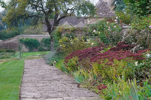 美しいイギリス風の風景庭園に開かれた石造りの夏の景色を眺め 花と緑の葉の植物が咲きます — ストック写真