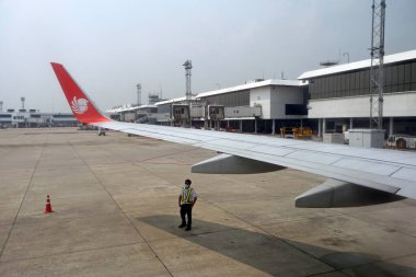 Maskeli adam uçak kanadının altında duruyor. Kabin penceresinden bak 