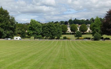 Güneşli bir yaz gününde yukarısı aydınlık gökyüzü olan bir kasaba parkında çimenlik alanda oynayan ferah yemyeşil bir manzaranın manzarası.