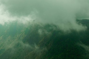 Dağların ya da tepelerin tepelerinden geçen puslu bulutlar. Sisli sabahta yeşil dağlar
