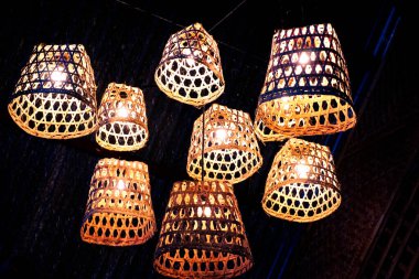 Close up view of traditional Indonesia woven bamboo lamp with yellow lamp in front of dark background