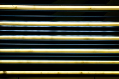 Horizontal pattern of yellow lamp with blue reflection accent in front of black background