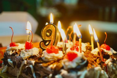 Ev yapımı 9. yaş günü pastası kutlaması. Büyük bir mum ve küçük mumlarla ortam aydınlanıyor. Yandan görüntüle.