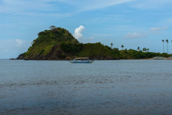 This photo captures the essence of the Philippines, with a traditional wooden boat bobbing on crystal-clear turquoise waters, surrounded by lush green tropical foliage. 