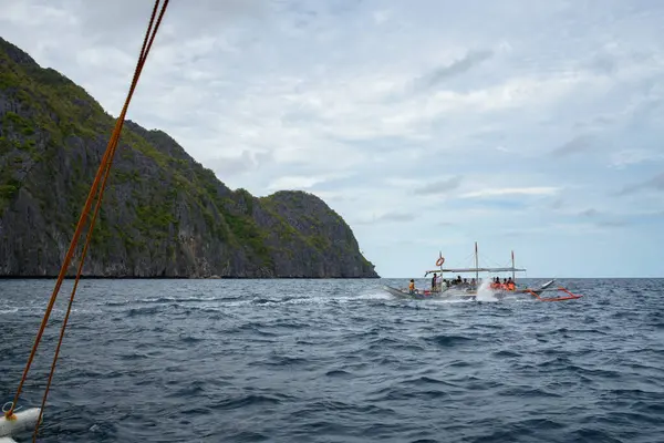 This photo captures the essence of the Philippines, with a traditional wooden boat bobbing on crystal-clear turquoise waters, surrounded by lush green tropical foliage. 