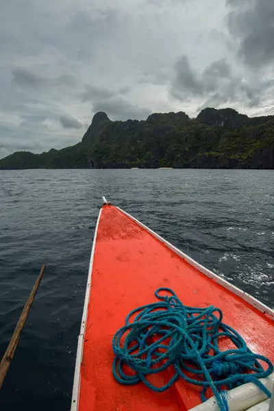 This photo captures the essence of the Philippines, with a traditional wooden boat bobbing on crystal-clear turquoise waters, surrounded by lush green tropical foliage. 