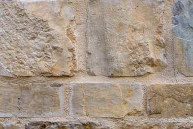 This close-up photo of a brick wall captures the rugged texture and earthy colors of the individual bricks. The rough surface of the bricks, with its cracks and crevices, is highlighted by the play of light and shadow. The warm, reddish tones of the 