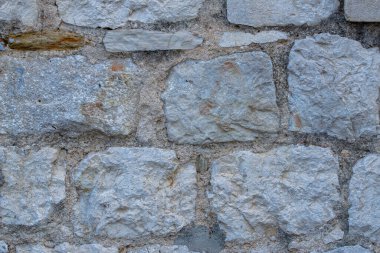 This close-up photo of a brick wall captures the rugged texture and earthy colors of the individual bricks. The rough surface of the bricks, with its cracks and crevices, is highlighted by the play of light and shadow. 