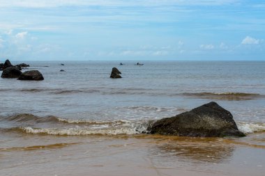 The photo captures a breathtaking view of a serene beach with crystal-clear waters and gentle waves lapping at the shore. The endless stretch of golden sand is dotted with sun umbrellas, beach chairs, and palm trees. The deep blue sea stretches out t