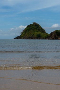 The photo captures a breathtaking view of a serene beach with crystal-clear waters and gentle waves lapping at the shore. The endless stretch of golden sand is dotted with sun umbrellas, beach chairs, and palm trees. The deep blue sea stretches out t