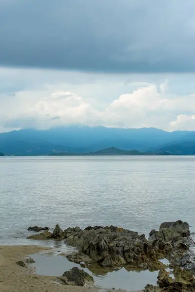 The photo captures a breathtaking view of a serene beach with crystal-clear waters and gentle waves lapping at the shore. The endless stretch of golden sand is dotted with sun umbrellas, beach chairs, and palm trees. The deep blue sea stretches out t
