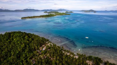 Fotoğraf, berrak suları ve kıyıya vuran hafif dalgalarla sakin bir sahilin nefes kesici görüntüsünü yakalıyor. Sonsuz altın kum taneleri güneş şemsiyeleri, plaj sandalyeleri ve palmiye ağaçları ile kaplıdır.. 