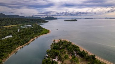 Fotoğraf, berrak suları ve kıyıya vuran hafif dalgalarla sakin bir sahilin nefes kesici görüntüsünü yakalıyor. Sonsuz altın kum taneleri güneş şemsiyeleri, plaj sandalyeleri ve palmiye ağaçları ile kaplıdır.. 