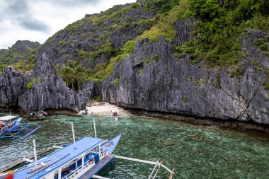 Fotoğrafta, sazdan çatılı canlı bir tropikal tekne güzel bir sahil ya da kayalık bir kıyıya demirli. Kristal berraklığında turkuaz su güneş ışığında parlar ve arka planda palmiye ağaçları yavaşça sallanır. Sahne mükemmel bir temsilci.