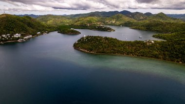 Fotoğraf, tropikal bir orman ya da dağ sırasının nefes kesici güzelliğini yakalar. Bereketli yeşil yapraklar ön planda hüküm sürerken, uzak mesafede, yüksek tepeler veya sis örtülü dağlar gökyüzüne karşı görkemli bir şekilde yükselir. Huzurlu sahne... 