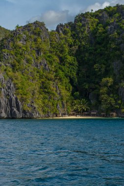Bu fotoğraf Filipin kıyılarının engebeli güzelliğini yansıtıyor. Ön planda yıpranmış kayalar turkuaz denizden fışkırırken, arka planda el değmemiş beyaz bir kumsal kıyı boyunca kıvrılır..