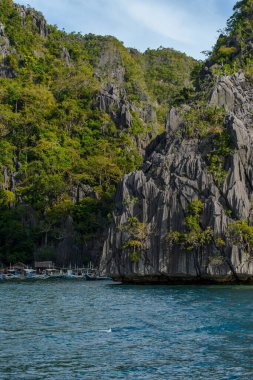 Bu fotoğraf Filipin kıyılarının engebeli güzelliğini yansıtıyor. Ön planda yıpranmış kayalar turkuaz denizden fışkırırken, arka planda el değmemiş beyaz bir kumsal kıyı boyunca kıvrılır..