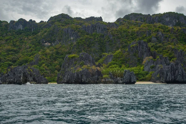 この写真はフィリピンの海岸線の険しい美しさを捉えています 前景には ターコイズブルーの海から風化した岩が飛び出し 背後には海岸沿いの自然のままの白い砂浜の曲線が描かれています — ストック写真