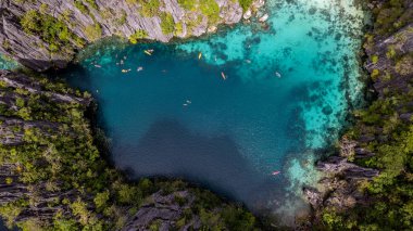Bu fotoğraf bir Filipinler lagününün ruhani güzelliğini yansıtıyor. Su, kayalık bir uçurum ve yeşil bir orman tarafından çerçevelenmiş turkuazın mükemmel bir gölgesidir. Sakin yüzey sadece ara sıra kano ya da raketlerle kırılır, ziyaretçiler gibi. 