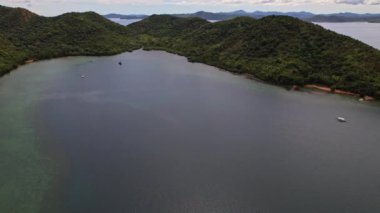 Filipinler, Coron 'daki sahil şeridinin insansız hava aracı görüntüleri. Dolly hareketi yaparız ve ormanlı deniz ve tepeleri görürüz..