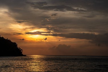 Gökyüzü karanlık ve bulutlu ve güneş batıyor. Su sakin ve gökyüzü bulutlarla dolu.