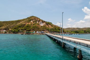 Okyanus manzaralı bir iskele gösteriliyor. Rıhtım yemyeşil bir yamaçla çevrili.