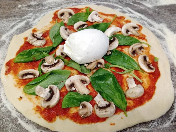 A raw Pizza dough. An Italian cuisine Pizza with tomato paste, Basil, Mushroom and Mozzarella cheese.