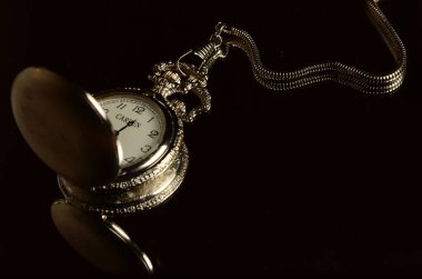 Siyah yansıtıcı yüzey üzerinde zinciri olan antika bir cep saatinin yakın çekimi..